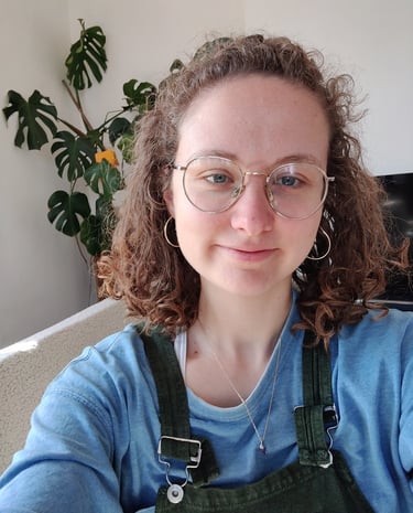 a selfie of Eleanor who is a curly haired queer women in her late twenties wtih glasses and dungarees