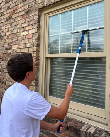 Eddie Sislo is using the squeegee tool to remove streaks from a window.