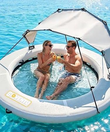 Couple relaxing in a large inflatable floating island pool with sunshade canopy in blue ocean water.