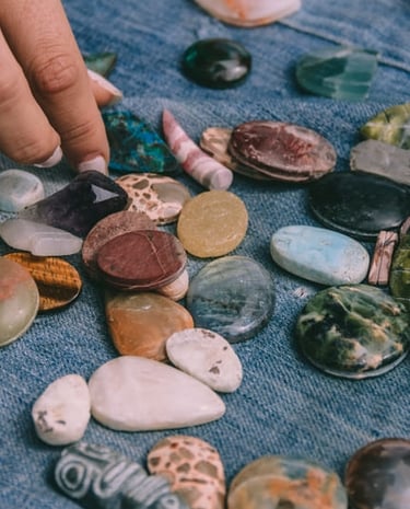 A hand selecting polished gemstones and healing crystals laid out on blue denim fabric.