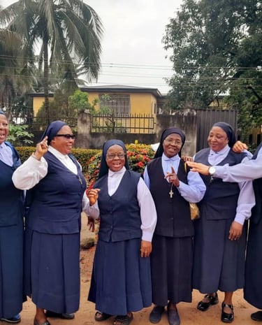 Six smiling Catholic nuns in blue and white habits posing outdoors together for a group photo.