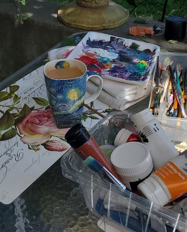 A photo of an artist's desk with all the necessary tools to paint including a big cup of coffee