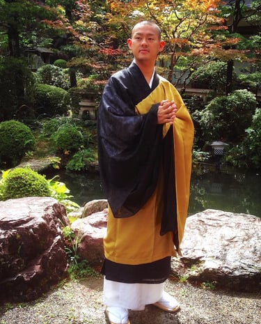 Buddhist monk in traditional yellow and black robes standing in a serene Japanese zen garden.