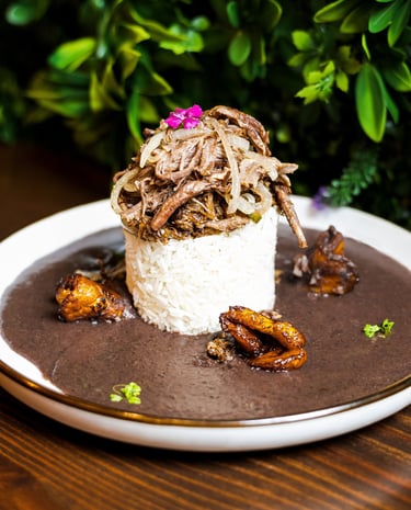 Gourmet Cuban Ropa Vieja served over white rice with black bean soup and fried plantains.