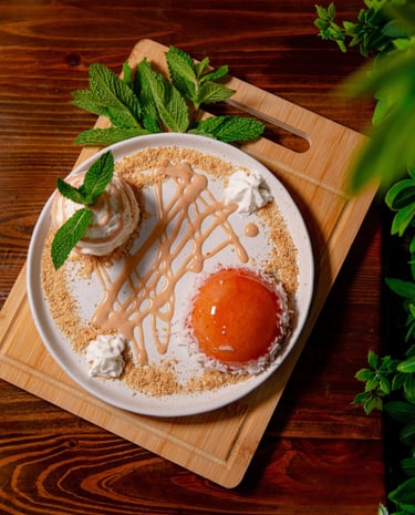 Gourmet peach dessert with fresh mint, cream, and crumble on a rustic wooden board.