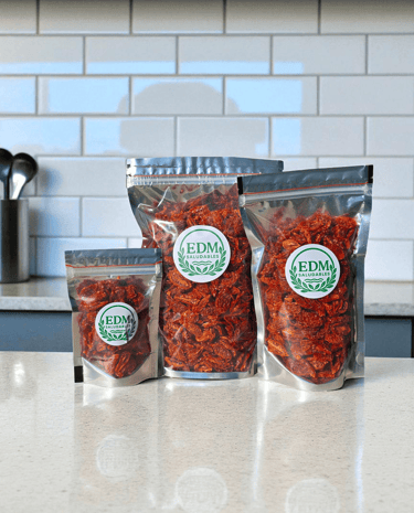 Tres tamaños de envases con tomates cherry deshidratados, sobre mesada de mármol.