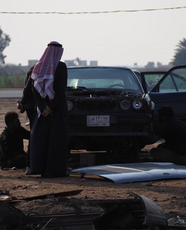 a group of Arab men in traditional clothes overlooking the dismantling of an old BMW