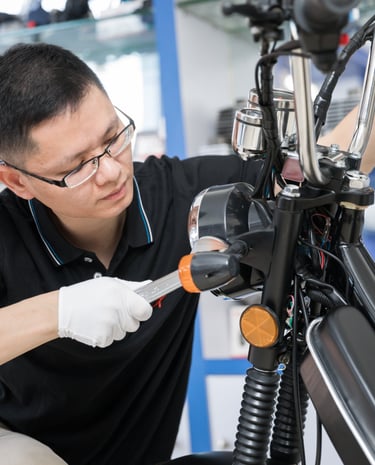 Professional mechanic wearing gloves and glasses repairing a motorcycle headlight in a shop.