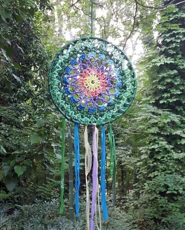 Dreamcatcher, hvatač snova nastao reciklažom plastičnih kesa, visi u zelenoj šumi. Simbol VATRE.