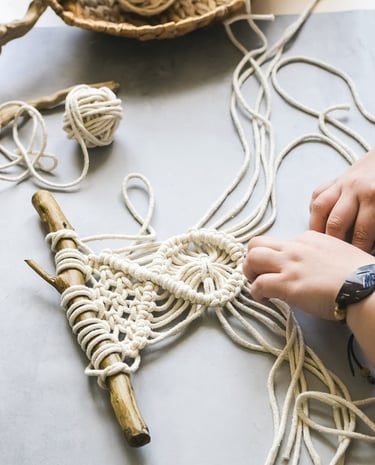 Manos elaborando un colgante de macramé DIY usando cuerda de algodón blanca y un palo de madera