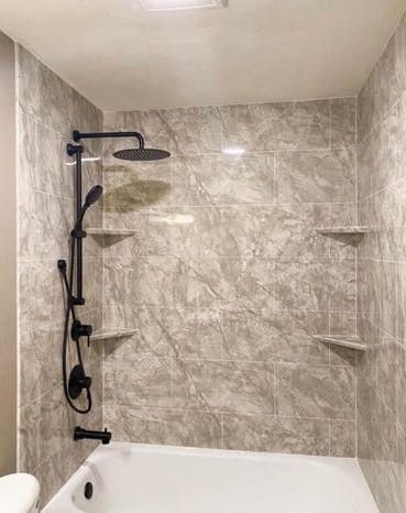 Elegant bathtub and shower combo featuring marble-look wall panels, matte black rainfall showerhead, and adjustable handheld 