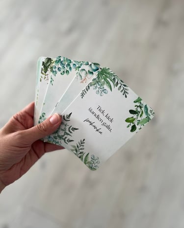Ranka laiko išskleistą afirmacijų kortelių rinkinį su žalių augalų iliustracijomis.