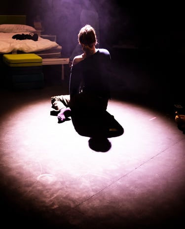 A white person, their back to the camera, seated in a pool of light