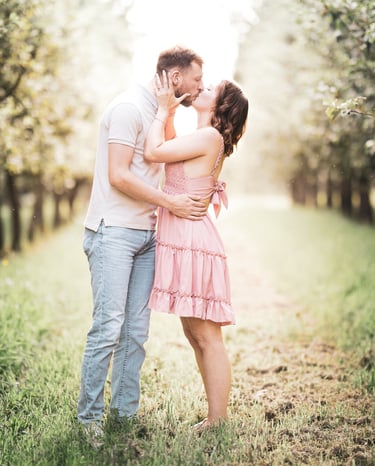 Couple kissing in a sunlit apple orchard during a romantic engagement photoshoot.