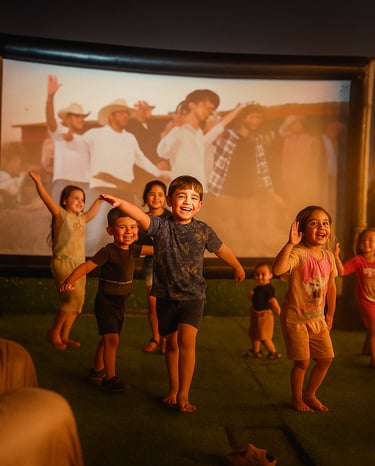 مجموعة من الأطفال الفرحين يلعبون ويرقصون أمام شاشة كبءرة في الهواء الطلق