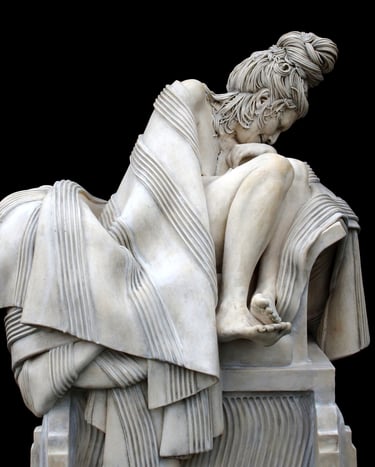 Closeup front of ceramic sculpture of grieving woman wrapped in blanket on large classical plinth.