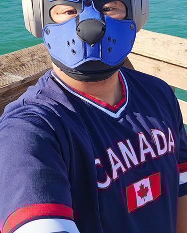 A Man in a pup mask with headphones standing on a pier.