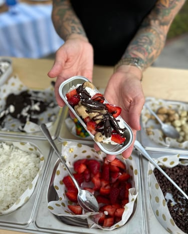 a person holding a dessert over a bar with topping options