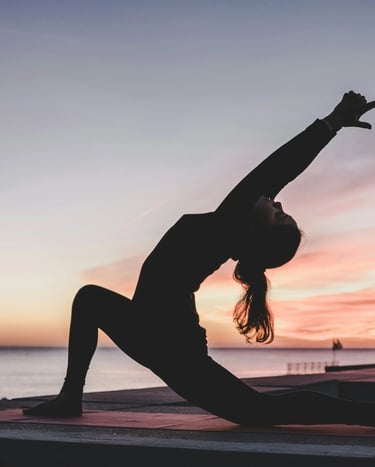 Woman practicing yoga at sunrise by the water, symbolizing peace and natural harmony