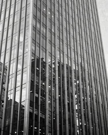A professional black and white architectural photograph of a sleek skyscraper in a North American / US city. The shot focuses on the geometric patterns of the glass facade, exuding contemporary elegance and clean, minimalist lines.
