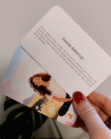 Psichologinės kortelės mamai su tekstu "sustok dabartyje" laikomos rankoje.