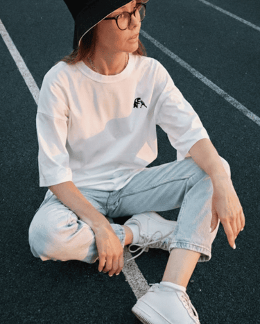Mujer con camiseta blanca y sombrero tipo pescador, usando tenis, en una pista de atletismo.