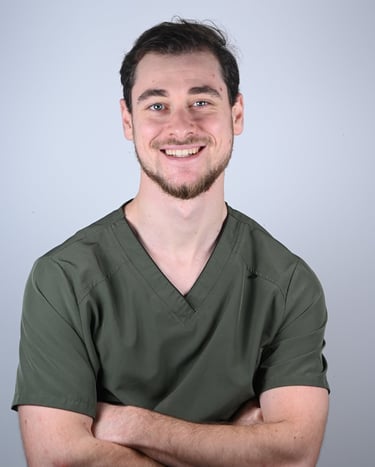 A smiling male healthcare professional wearing olive green medical scrubs with arms crossed.