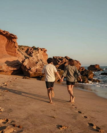 A beautiful documentary lifestyle photo of a couple running hand-in-hand along a rugged Spanish coastline. Warm sand and terracotta rock formations in the background, with the golden hour sun casting long shadows, creating a nostalgic, cinematic mood.