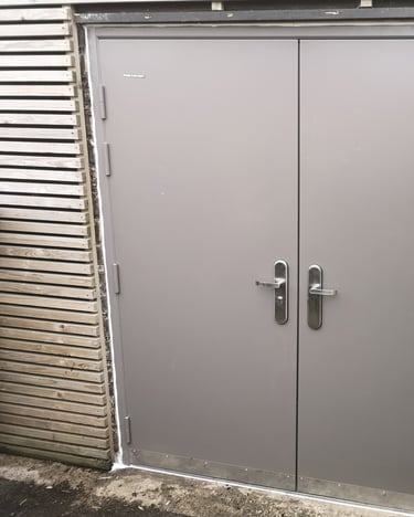 Durable grey steel double security doors installed between a brick wall and wooden fencing.