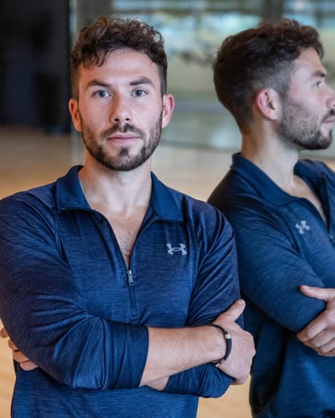 Professional male fitness trainer in blue athletic wear posing in a gym studio with mirror reflection.