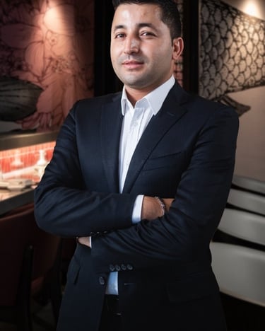Professional male entrepreneur in a navy suit posing in a modern restaurant setting.