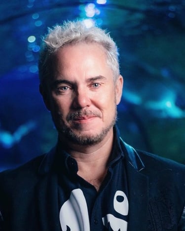 Portrait of a man with spiky blonde hair and a goatee in a blue lit underwater tunnel aquarium.