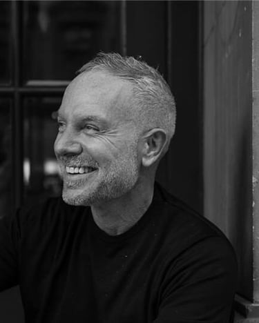 A black and white portrait of a smiling middle-aged man with short gray hair and a beard.