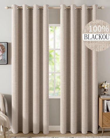 Beige 100% blackout curtains with grommets hanging on a wooden rod over a living room window.