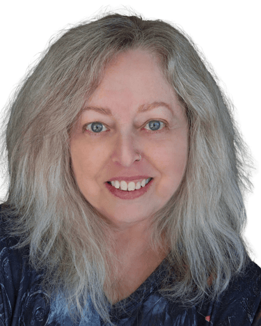 A middle aged woman with green eyes and blonde hair and wearing a grey patterned top