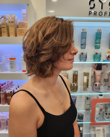 Side profile of a woman with a layered, wavy light brown bob haircut in a professional hair salon.