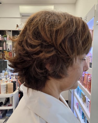 Side profile of a woman with a layered, honey-brown shag haircut and flipped ends in a professional hair salon.