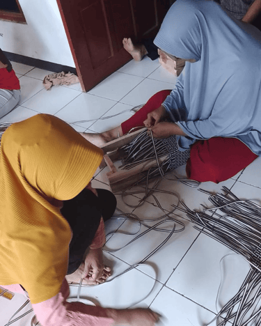 Handmade jali jali woven bag frame being prepared by artisans using recycled plastic weaving strips.