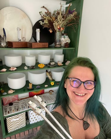 Smiling lady holding a tuning fork and sound bowls behind her