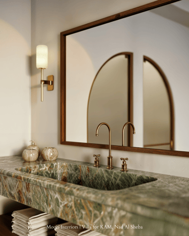 Close-up of green stone sink with bronze tap, wall sconce, and arched mirror reflection.