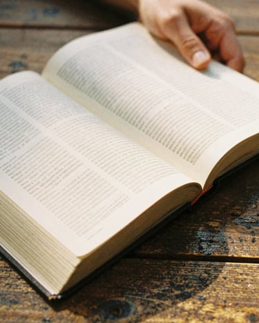 Close-up of hands holding an open Bible on a rustic wooden table, warm golden hour light illuminating the pages, shallow depth of field, 35mm film look