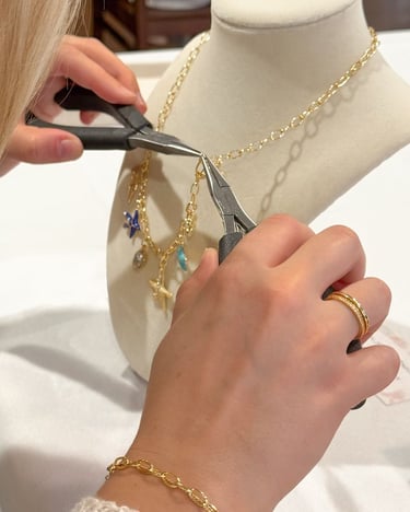 Artesana utilizando pinzas para colocar un dije en un collar de cadena dorada