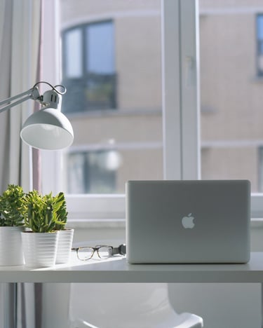 Modern home office desk with a laptop, desk lamp, green plants, and eyeglasses