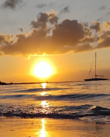 a sunset on a beach with sailboats in the background