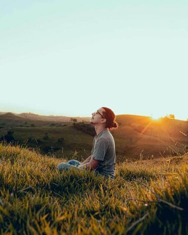 Person sitting in a field at sunset with head lifted in prayer.