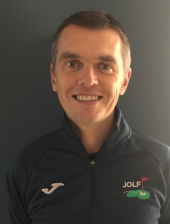 Portrait of a person wearing a navy quarter-zip sports top with a golf logo, smiling at the camera