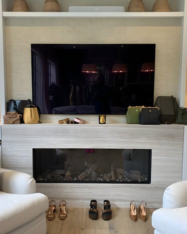A refined display of luxury handbags and shoes by London stylist arranged along a fireplace ledge.