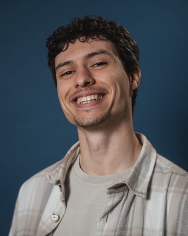 A smiling young man with curly hair and a plaid shirt posing against a blue background.