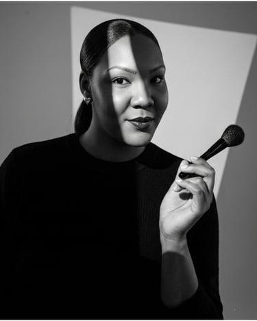 Professional makeup artist holding a powder brush in a black and white studio portrait.