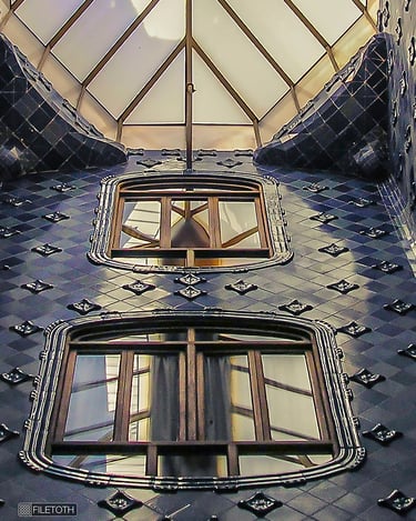 View upward through Casa Batlló’s tiled light well where daylight cascades toward the central skylight.